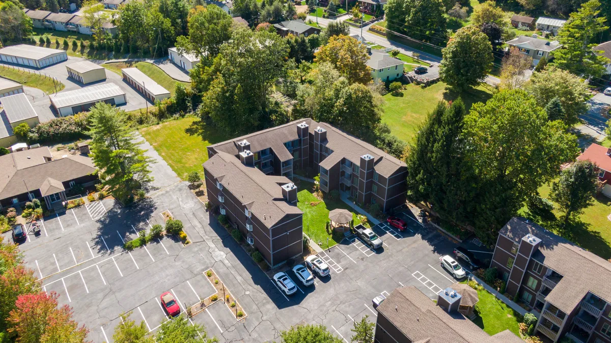 This exterior shot features the Bear Pause apartment buildings set amid green spaces and mature trees, with a visible parking lot in the foreground. The inviting lawn and surrounding landscape hint at outdoor leisure opportunities and the property's connection to nature.