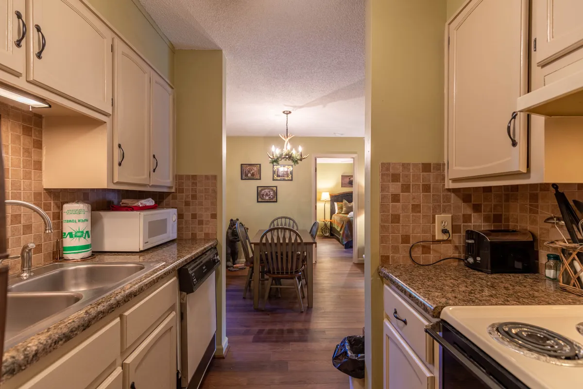A view focusing on the kitchen sink and adjacent dining table, illuminated by a warm light fixture. The setting suggests active cooking, dining, and socializing, creating an inviting mood for family traditions and intimate meals.