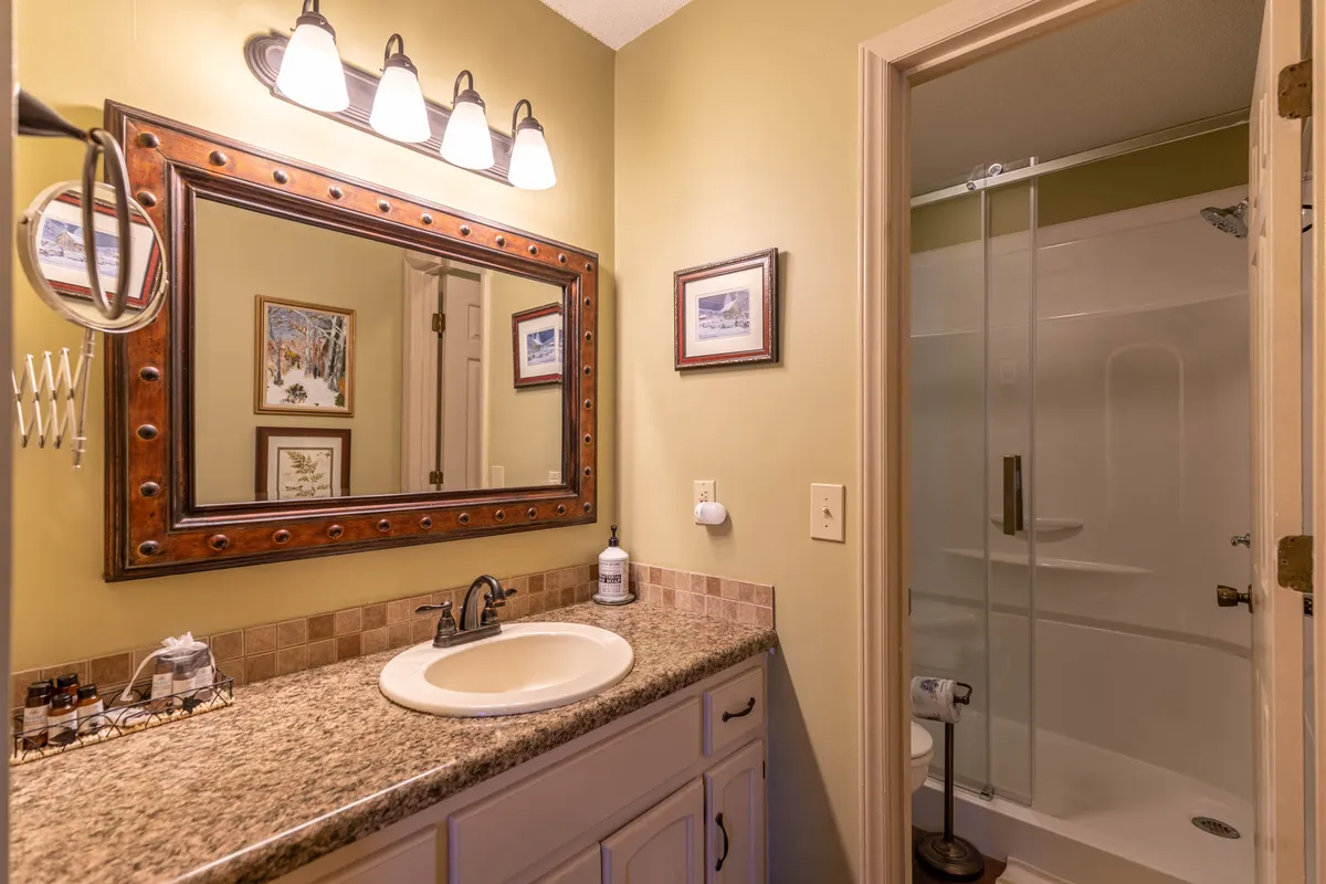 A modern ensuite bathroom with a large mirror, granite countertop, framed pictures, and a shower area. The space feels calm and refreshing, suggesting a peaceful place to prepare for the day or unwind at night.