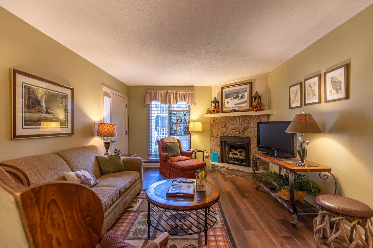 This inviting view centers on the plush sofa and stone fireplace, complemented by a cozy coffee table and soft lamp lighting. The arrangement encourages relaxation and socializing, highlighting the warmth of the hearth and the room's comfortable seating.