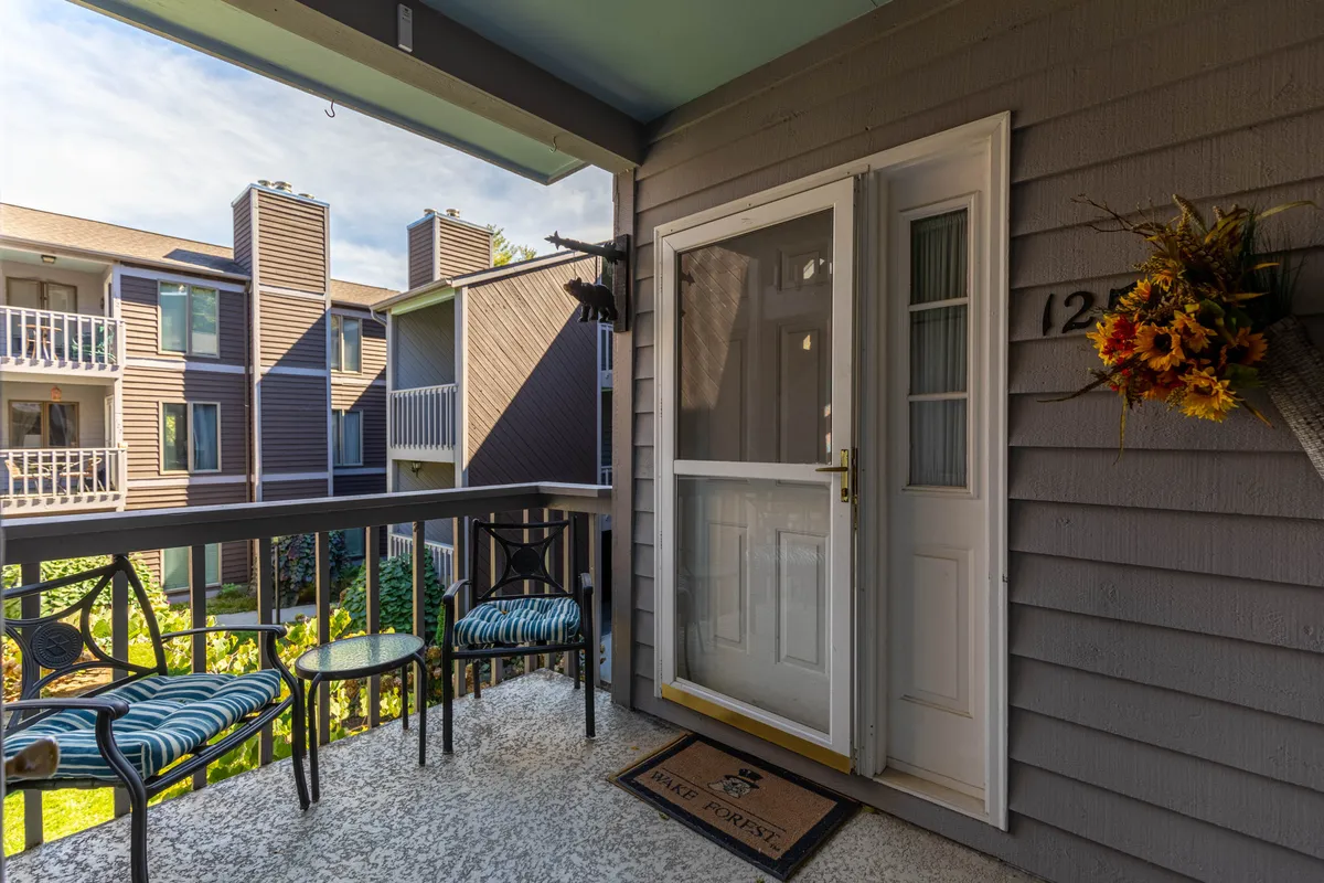 The image shows the front entrance of a condo with a small set of table and chairs arranged on the porch, accompanied by a decorative flower arrangement. This inviting setup suggests a welcoming space perfect for morning coffee or relaxing after exploring the town.