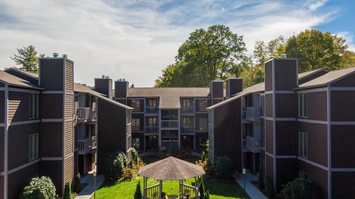 The image showcases the exterior of a charming condo building nestled among landscaped gardens, with a picturesque gazebo set amid lush greenery. Sunset light bathes the balconies, hinting at peaceful evening views, while the inviting gazebo suggests a perfect spot for gatherings or relaxation.