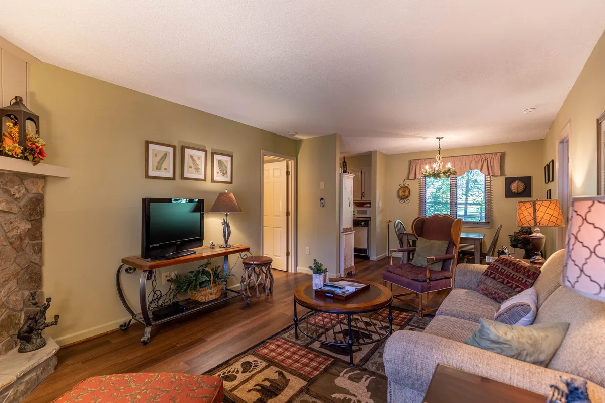 This image captures the heart of the living area, featuring a cozy stone gas-log fireplace, cable television, and an inviting dining table with decorative wall art and warm lighting. The open-concept space is arranged for both relaxing evenings and lively gatherings, with ample natural light streaming in through the windows.