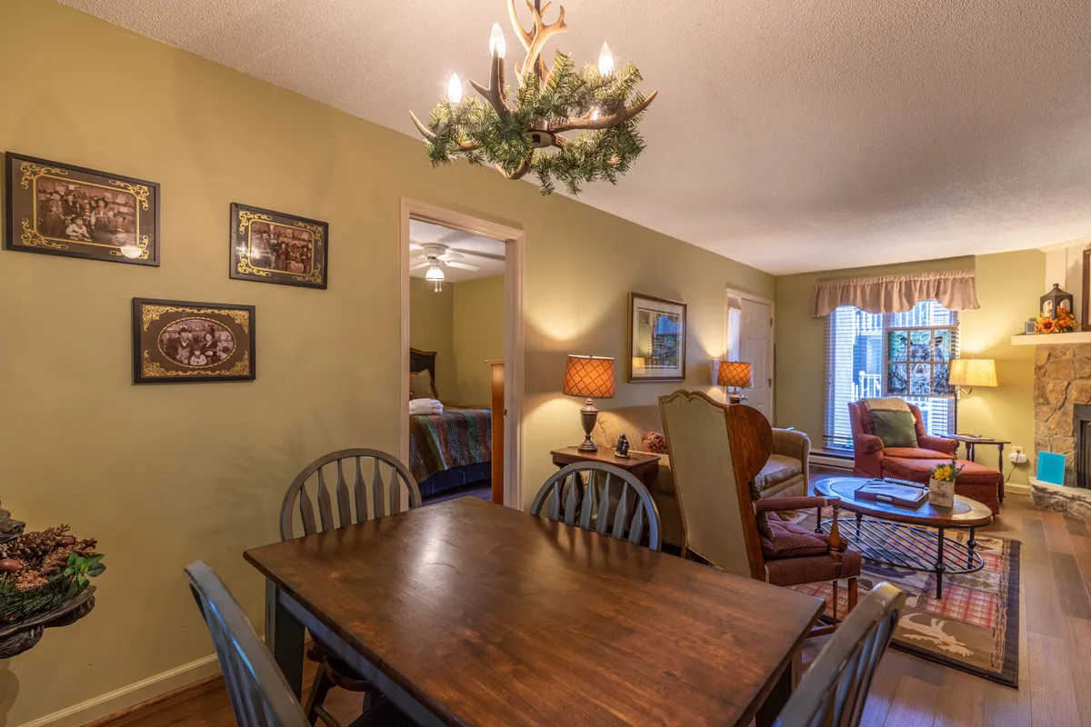 This image spotlights the dining table set beside the stone fireplace, with comfortable seating, a stylish chandelier, and framed pictures enhancing the cozy atmosphere. The scene invites both relaxed dining and quiet moments by the fire.