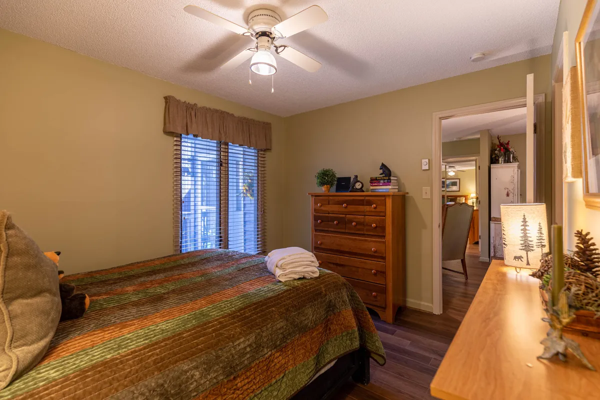 A tranquil bedroom with a quilted bed, a dresser, and a window with blinds letting in natural light, providing a peaceful retreat.